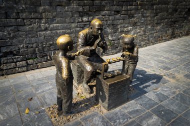 Xiangyang, Hubei, Çin - 20 Mart 2018: Yaşlı bir zanaatkar oyuncağını izleyen iki çocuğun öğrenme ve büyülenme anını yakalayan bronz bir heykel.