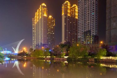 Wuhan, Çin - 21 Mart 2018: Yanxia Köprüsü yakınlarındaki parlak gökdelenler durgun suya güzel bir şekilde yansıdı. Şehrin canlı gece hayatını gösteriyoruz..