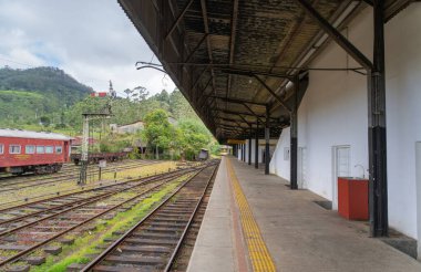 Gözü yemyeşil dağlara götüren boş rayları olan sakin bir tren istasyonu. Bir kırmızı tren dinleniyor, durgunluk hissi uyandırıyor. Ambewela, Sri Lanka.