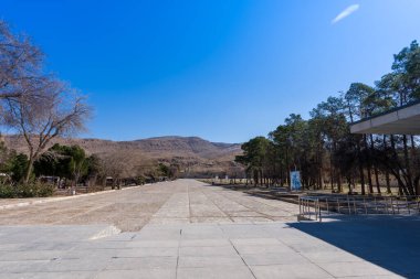 Ulusal bayraklar ve sembolik amblem ile süslenmiş girişi büyüleyici bir şekilde görmek. Berrak mavi gökyüzünün altında yemyeşil ortamda. Persepolis, İran.
