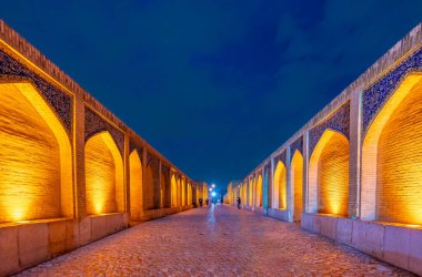 Tarihi Khaju Köprüsü, alacakaranlıkta derin mavi gökyüzünün altında parlak turuncu ışıklarla parlar. Pers mimarisinin sembolü, İsfahan, İran.