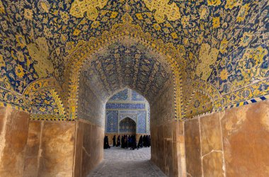 İsfahan, İran - 5 Mart 2024: İran fayanslarıyla süslenmiş kemerli bir koridor İmam Camii 'nde güzel dekore edilmiş bir odaya açılıyor. Turistler toplanıyor..