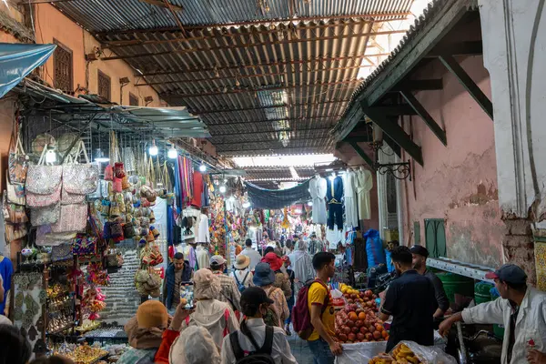 emaa el-Fnaa, Marakeş, Fas - 18 Mart 2024: Yerli ve turistlerin gölgeli bir sokak altında geleneksel mallar için alışveriş yaptığı hareketli bir pazar yeri.