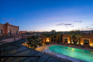 Ouarzazate, Fas - 19 Mart 2024: Geleneksel Fas mimarisini yansıtan sakin otel havuz kenarına çöküyor.