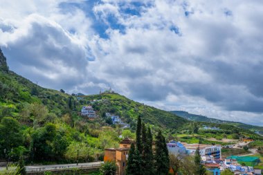 Arka planda yeşil dağlar olan panoramik kır evi manzarası. Canlı yeşillik mimariyle keskin bir tezat oluşturuyor. Şef, Fas..