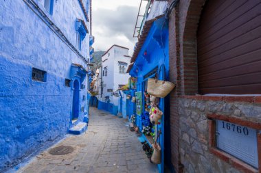 Chefchaouen, Fas - 25 Mart 2024: Mavi boyalı sokaklarda renkli seramik tabaklar ve aynalar sergilenen bir el işi dükkanı.