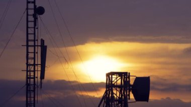 Radar istasyonu üzerinde parlak turuncu ve mor renkleri olan çarpıcı bir gün batımı. Siluetli iletişim kuleleri ve antenler renkli gökyüzüne karşı duruyor. Caoshan Radar İstasyonu, Tayvan.