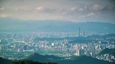 Taipei şehrinin panoramik manzarası. Şehir uzaklığa doğru uzanıyor ve manzara yuvarlanan tepeler ve gökyüzündeki tüylü bulutlarla çevrili. Yeni Tayvan Şehri, Tayvan.