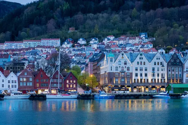 Bergen, Norveç - 30 Nisan 2024: Bergen, Norveç 'in renkli ahşap binalarıyla ikonik Bryggen rıhtımı insanlarla dolup taşıyor. Rıhtıma yanaşan tekneler büyüleyici manzarayı daha da güzelleştiriyor..