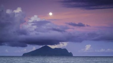 Dolunay, Kaplumbağa Adası 'nın huzurlu gece manzarasını aydınlatıyor. Gökyüzü mor ve mavinin değişik tonlarında dramatik bulutlarla doluydu. Touzhen, Yilan County, Tayvan.