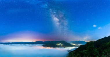 Samanyolu, bulutlar denizi üzerindeki yıldızlı gece gökyüzünde uzanır. Bu nefes kesicidir. Uzak kasabaların ışıkları huzurlu manzaraya biraz sıcaklık katar. Xindian Bölgesi, Tayvan.