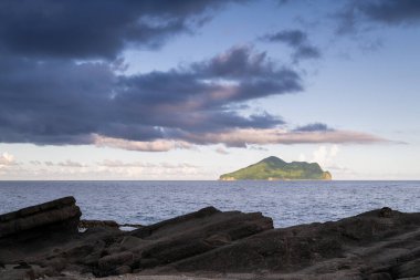 Kaplumbağa Adası 'nın denizdeki yemyeşil bitkilerle kaplı uzak manzarası. Beyaz bulutlar yavaşça yukarı doğru sürüklenerek adaya gölge düşürüyor. Şaşırtıcı doğal manzara, Yilan County, Tayvan.