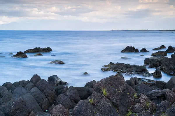 stock image Rocky coastline with a clear blue ocean and white clouds drifting in a blue sky. Scenic coastal view, Yilan County, Taiwan.