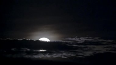 Parlak bir dolunay bulutların ardında zarafetle beliriyor. Ruhsal ışıltısı gece gökyüzünü aydınlatıyor, dingin ve mistik bir atmosfer yaratıyor..