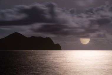 Dolunay, Kaplumbağa Adası 'nın huzurlu gece manzarasını aydınlatıyor. Gökyüzü mor ve mavinin değişik tonlarında dramatik bulutlarla doluydu. Touzhen, Yilan County, Tayvan.