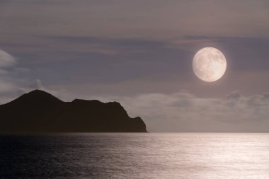 Dolunay, Kaplumbağa Adası 'nın huzurlu gece manzarasını aydınlatıyor. Gökyüzü mor ve mavinin değişik tonlarında dramatik bulutlarla doluydu. Touzhen, Yilan County, Tayvan.