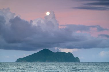 Dolunay, Kaplumbağa Adası 'nın huzurlu gece manzarasını aydınlatıyor. Gökyüzü mor ve mavinin değişik tonlarında dramatik bulutlarla doluydu. Touzhen, Yilan County, Tayvan.