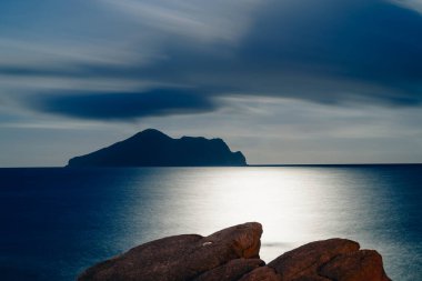 Dolunay, Kaplumbağa Adası 'nın huzurlu gece manzarasını aydınlatıyor. Gökyüzü mor ve mavinin değişik tonlarında dramatik bulutlarla doluydu. Touzhen, Yilan County, Tayvan.
