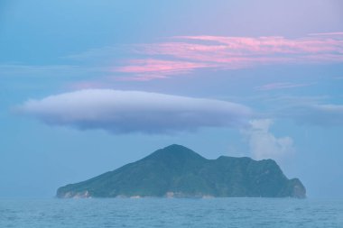 Kaplumbağa Adası üzerinde yalnız bir bulut sürükleniyor, adanın engebeli kıyı şeridine yumuşak ve sıcak bir parıltı saçıyor. Pasifik Okyanusu 'nun yüzeyi sakin ve yansıtıcıdır. Yilan County, Tayvan.