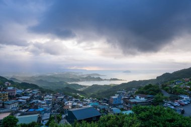 Dağın tepesinden, dumanla örtülü bir manzara beliriyor ve yuvarlanan tepelerin arasına yerleşmiş pitoresk bir kıyı köyünü gösteriyor. Jiufen, Tayvan.