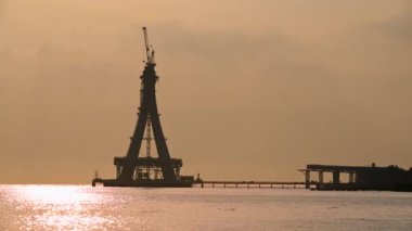 Tamsui Köprüsü 'nün inşaat halindeki görkemli bir silueti gün batımının altın renklerinde yıkanır. Bitmemiş yapı canlı bir gökyüzüne karşı dimdik ayakta duruyor. Tamsui, Tayvan.