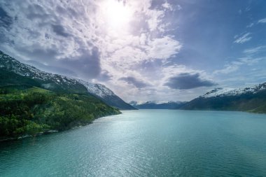 Hardangerfjord 'un sakin bir manzarası. Turkuaz sular etrafındaki karlı dağları ve yemyeşil ormanları yansıtır. Rahatlamak ve kaçmak için mükemmel huzurlu bir manzara. Voss, Norveç.