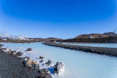 Milky blue waters of the Blue Lagoon in Iceland contrast with black lava rocks and lichen; a peaceful geothermal spa scene. Reykjanes Peninsula, Iceland. clipart