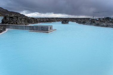 İzlanda 'daki Mavi Göl' ün süt mavisi suları siyah lav kayaları ve liken ile tezat oluşturur; barışçıl bir jeotermal kaplıca sahnesi. Reykjanes Yarımadası, İzlanda.