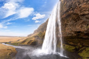 Görkemli Seljalandsfoss şelalesi buzulların eriyen sularından oluşur. Onu eşsiz yapan şelalenin arkasındaki ulaşılabilir iz. Reykjavik Yarımadası, İzlanda.