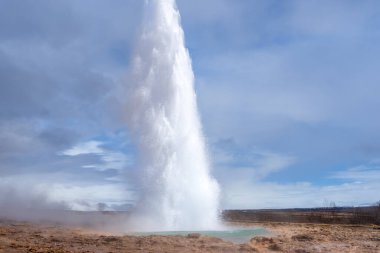 Turistler, Strokkur gayzerinin patlamasına hayret ederek havaya buhar ve su bulutu gönderiyorlar. Bu jeotermal harikalar İzlanda 'da popüler bir cazibedir. Geysir Jeotermal Alanı, İzlanda.