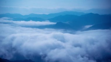 Hilal ay ve yıldızlı bir gece gökyüzünün altındaki bulutların nefes kesici panoramik görüntüsü. Uzak dağların silueti bu sakin manzaraya derinlik ve dram katıyor. Xindian, Tayvan.