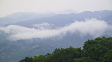 Yuvarlanan tepelerin sakin manzarası yemyeşil bitki örtüsüyle kaplı, bulutlardan oluşan bir deniz yukarda yavaşça sürükleniyor. Sisli atmosfer huzur ve huzur hissi yaratıyor. Xindian Bölgesi, Tayvan.