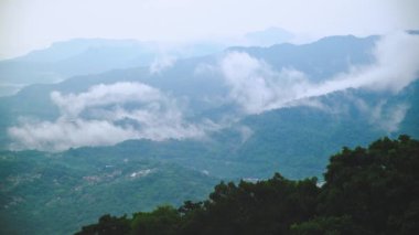 Bulutların arasından bakan uzak dağların olduğu sisli bir vadinin nefes kesici manzarası. Yeşillik ve yumuşak, doğal ışık güzel ve sakinleştirici bir sahne yaratır. Xindian, Tayvan.