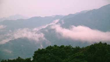 Puslu, yemyeşil bir vadinin nefes kesici manzarası. Bulutlar yumuşak, ruhani bir atmosfer yaratırken uzak dağlar dramatik bir zemin oluşturuyor. Xindian, Tayvan.