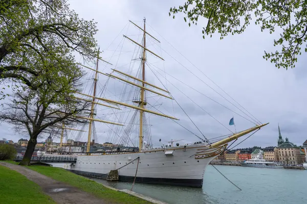 Görkemli bir beyaz yelkenli gemisi Stockholm limanına yanaşıyor ve arkasında şehrin silüeti var. Stockholm, İsveç.