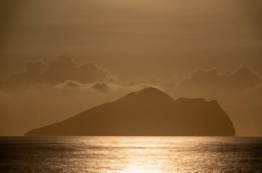 Tayvan, Yilan 'daki ikonik Kaplumbağa Adası' nın arkasında büyüleyici bir ay yükselişini gösteren, yumuşak dalgalı sakin bir okyanus sahnesi. Ay bulutların arasında zarif bir şekilde dans eder..