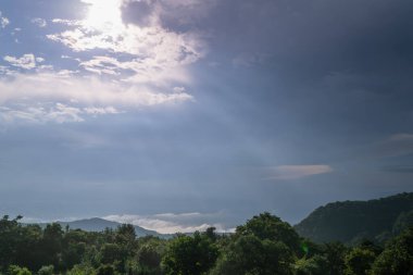 Taipei şehrinin kısmen bulutlarla kaplı siluetinin nefes kesici panoramik görüntüsü. Altın güneş ışınları bulutlu gökyüzünü delip geçer ve şehir manzarasına sıcak bir ışık saçar. Tayvan.