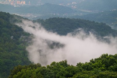 Puslu, yemyeşil bir vadinin nefes kesici manzarası. Bulutlar yumuşak, ruhani bir atmosfer yaratırken uzak dağlar dramatik bir zemin oluşturuyor. Xindian, Tayvan.