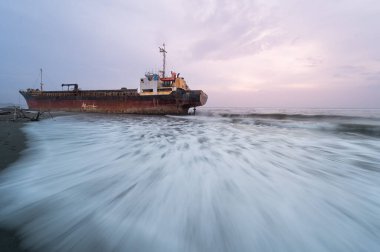 Issız terk edilmiş bir gemi Xigushui Sahili kıyısında, esrarlı bir geçmişi ima eden yıpranmış gövdesi ve pas lekeli güvertesi. Batan güneş sahnenin üzerine sıcak bir parıltı saçıyor. Tainan..