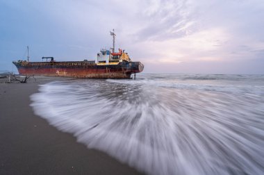 Issız terk edilmiş bir gemi Xigushui Sahili kıyısında, esrarlı bir geçmişi ima eden yıpranmış gövdesi ve pas lekeli güvertesi. Batan güneş sahnenin üzerine sıcak bir parıltı saçıyor. Tainan..