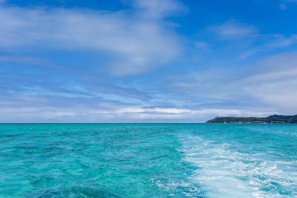 Sailboats glide across the crystal-clear turquoise waters of Ile aux Cerfs, Mauritius. The gentle waves create a ripple effect behind the boats. Ile aux Cerfs, Mauritius, Indian Ocean.