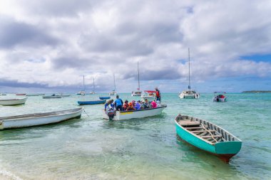 Ile Aux Cerfs, Mauritius - 8 Eylül 2024: Turistler, adanın manzaralı manzarasını seyrederek tekne turnesinin keyfini çıkarırken görülüyor. Turkuaz sularda birkaç tekne ve yat demirlemiş..
