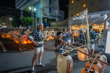 Akita, Japonya - 5 Ağustos 2024: Genç katılımcılar tecrübeli yaşlıların rehberliğinde şehrin sokaklarında büyük Kanto fenerleri taşıyorlar. Şenlikli atmosfer çok canlı..
