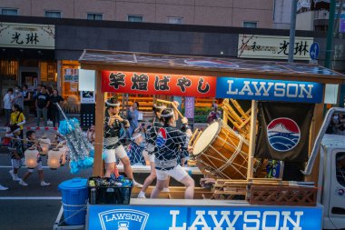 Akita, Japonya - 5 Ağustos 2024: Genç kadınlar Akita Kanto Festivali sırasında bir festival şamandırasında davul ve flüt çalıyorlar. Kalabalık neşeli atmosfere tezahürat yaptı ve ekledi..