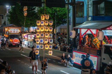 Akita, Japonya - 5 Ağustos 2024: Genç katılımcılar tecrübeli yaşlıların rehberliğinde şehrin sokaklarında büyük Kanto fenerleri taşıyorlar. Şenlikli atmosfer çok canlı..