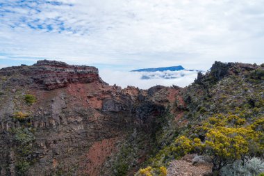 A close-up view of a volcanic crater on Piton de la Fournaise, Reunion Island. The steep, rugged walls of the crater are covered in lush vegetation, contrasting with the barren, rocky interior. clipart