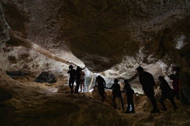 Turistler, ayak altında derin bir vadi bulunan dar kireçtaşı mağaralarda gezinirler. Karst oluşumları ve ağaç kökleri eşsiz bir manzara yaratır. Bemaraha Ulusal Parkı, Madagaskar.