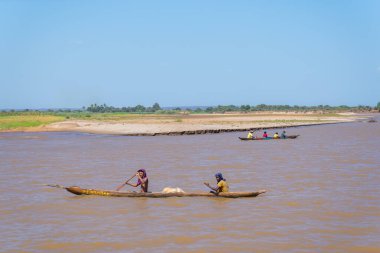 Manambolo Nehri, Madagaskar - 28 Ağustos 2024: İki balıkçı, kanonun ortasına yerleştirilmiş beyaz bir ağla balık tutmaya hazırlanan, sarımsı bir nehirde bir kano yüzdürür..