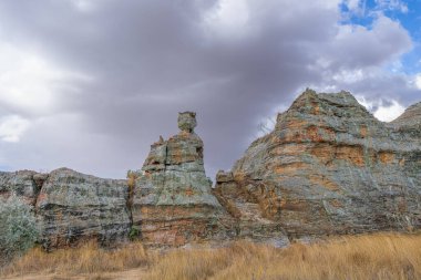 Dramatik bulutlu gökyüzünün altında tacı andıran ikonik Isalo Kum Taşı oluşumu kraliçesi. Çimlerle çevrili doğal dayanmış kireçtaşı uçurumları. Isalo Ulusal Parkı, Madagaskar.