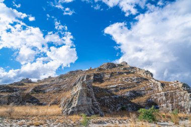 Dramatik katmanlı kumtaşı kayalıkları, parlak mavi gökyüzünün altında, dağınık beyaz bulutlarla kuru savananın üzerinde yükseliyor. Isalo Ulusal Parkı, Madagaskar 'da Jurasik jeolojik oluşumlar.